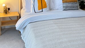 Een slaapkamer met een bed, nachtkastje, lamp, macramé wanddecoraties, potplanten en een groene wand.