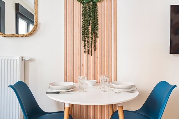A dining area with a round table, two blue chairs, white plates, and glasses.