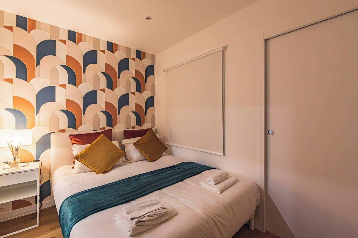 Une chambre d’hôtel avec un lit, une table de chevet, un mur orné d’un motif géométrique et une porte.