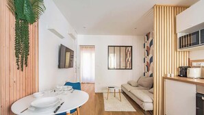 A modern living space with a dining area, a sofa, a kitchen, and a television.