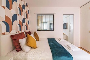 A hotel room with a bed, pillows, a window, a mirror, and a wardrobe.