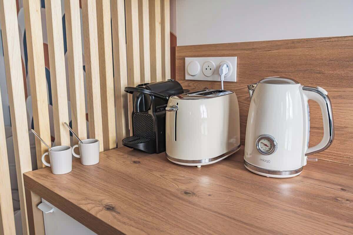 A kitchenette with a coffee maker, toaster, and kettle on a wooden countertop.