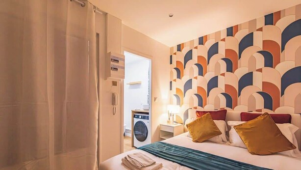 A hotel room with a bed, a washing machine, and a patterned wall.