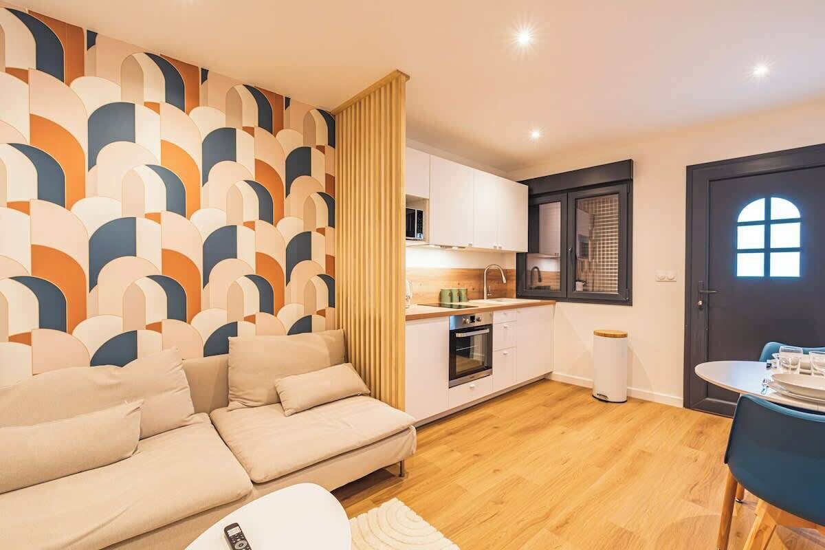 Een moderne woonkamer met een bank, een eettafel met stoelen, een keuken met kasten en apparatuur, en een behang met patroon.