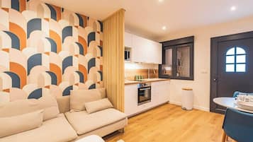 Een moderne woonkamer met een bank, een eettafel met stoelen, een keuken met kasten en apparatuur, en een behang met patroon.