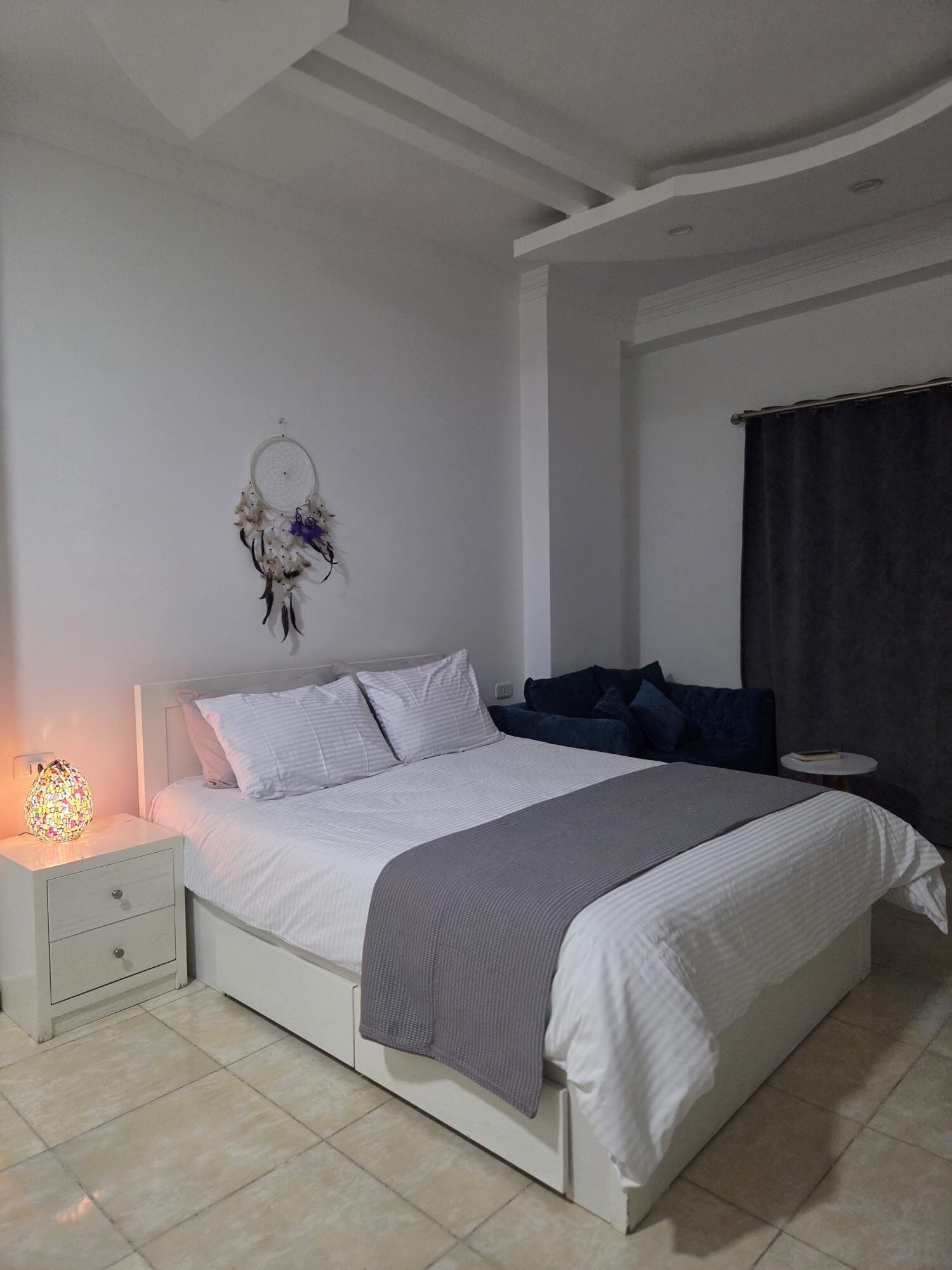 Ein Schlafzimmer mit Bett, Nachttisch und einem Traumfänger an der Wand.