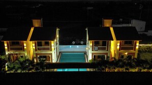A two-story building with a swimming pool in the center, surrounded by well-lit balconies and a landscaped garden. - XYLEM SEA SIDE RESORT (Brahmagiri)