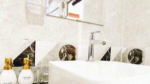 Une salle de bain moderne avec un lavabo blanc, deux flacons de couleur dorée et un grand miroir.