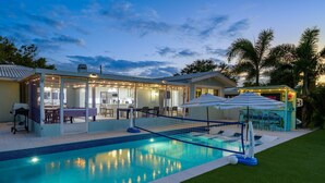 A swimming pool with a covered patio area, a small kiosk, and a lawn. - Waterfront • Walk to Beach • Pool • Kayaks • Bikes (Indian Rocks Beach)