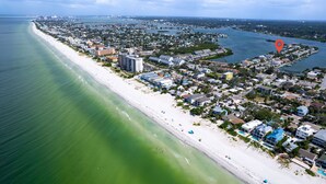 An aerial view of a coastal town with a long sandy beach, residential buildings, and a marina. - Waterfront • Walk to Beach • Pool • Kayaks • Bikes (Indian Rocks Beach)