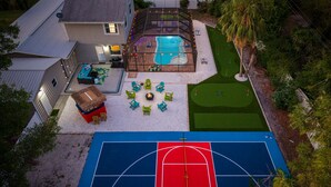 En baghave med basketballbane, swimmingpool og en terrasse med udendørs møbler.