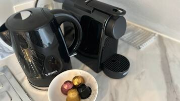 Una cafetera, una jarra de vidrio y un bol con cápsulas de café sobre una encimera de mármol.
