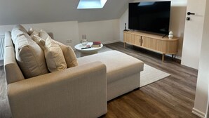 A modern living room with a sectional sofa, a TV on a wooden cabinet, and a skylight. - Cozy 1BR plus LR Apt Ghent Gravensteen (Ghent)
