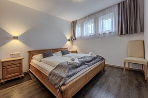 A double bed with a wooden frame, two bedside tables, a chair, and a window with curtains.