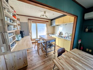 A kitchen with wooden flooring, a dining area with stools, and a window with curtains.
