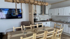 Eine moderne Küche mit weißen Schränken, einem Holztisch mit Stühlen und einem an der Wand befestigten Fernseher.