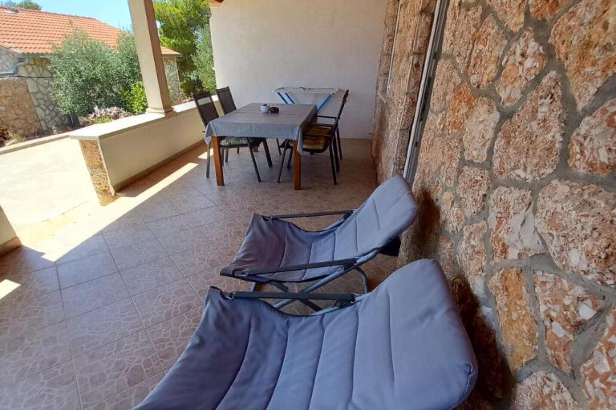 A patio area with a table and chairs, a stone wall, and two lounge chairs.