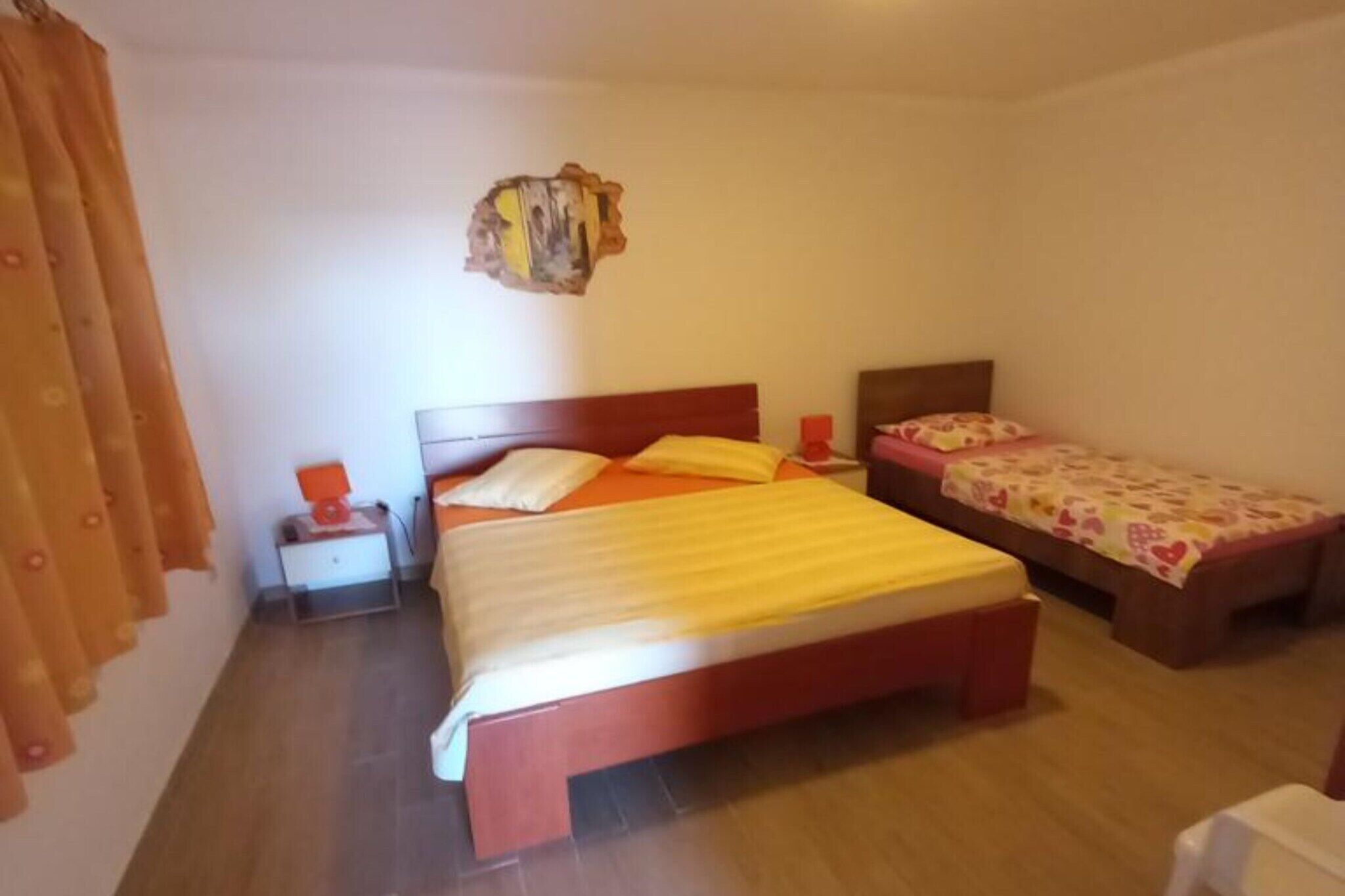 A bedroom with a large bed, a smaller bed, a nightstand, and a wall-mounted decoration.