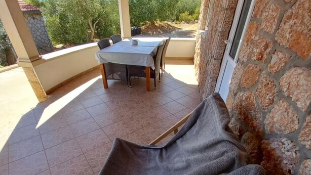 A covered patio area with a table and chairs, stone walls, and a view of greenery. - Comfort One Bedroom Apartment with Terrace and Sea view (Sveta Nedjelja)