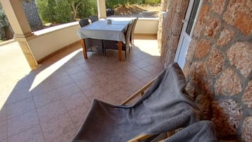 A covered patio area with a table and chairs, stone walls, and a view of greenery.