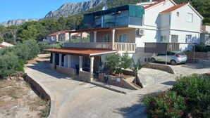 A two-story house with a balcony, a car parked in front, and a mountainous backdrop. - Comfort One Bedroom Apartment with Terrace and Sea view (Sveta Nedjelja)