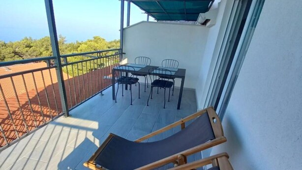 A balcony with a table and chairs, a wooden chair, and a view of greenery. - One Bedroom Apartment with Balcony and Sea View (Sveta Nedjelja)