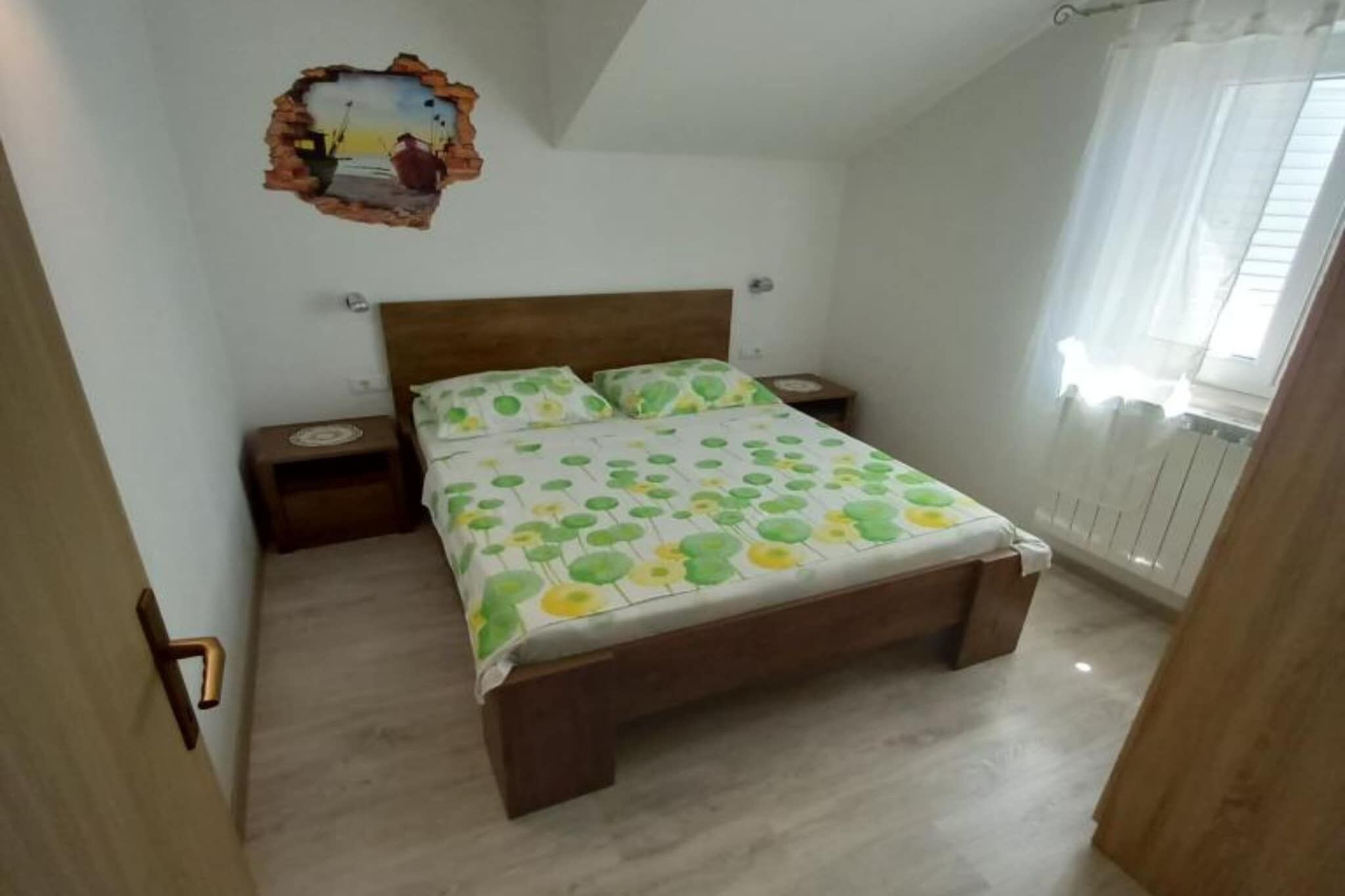 A bedroom with a wooden bed, a nightstand, a wall decoration, and a window with curtains.