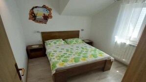 A bedroom with a wooden bed, a nightstand, a wall decoration, and a window with curtains. - One Bedroom Apartment with Balcony and Sea View (Sveta Nedjelja)