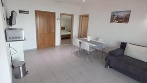 A modern living room with a gray sofa, a dining table with chairs, a TV, and a trash can. - One Bedroom Apartment with Balcony and Sea View (Sveta Nedjelja)
