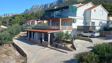 A two-story house with a balcony, a car parked in front, and a mountainous backdrop.