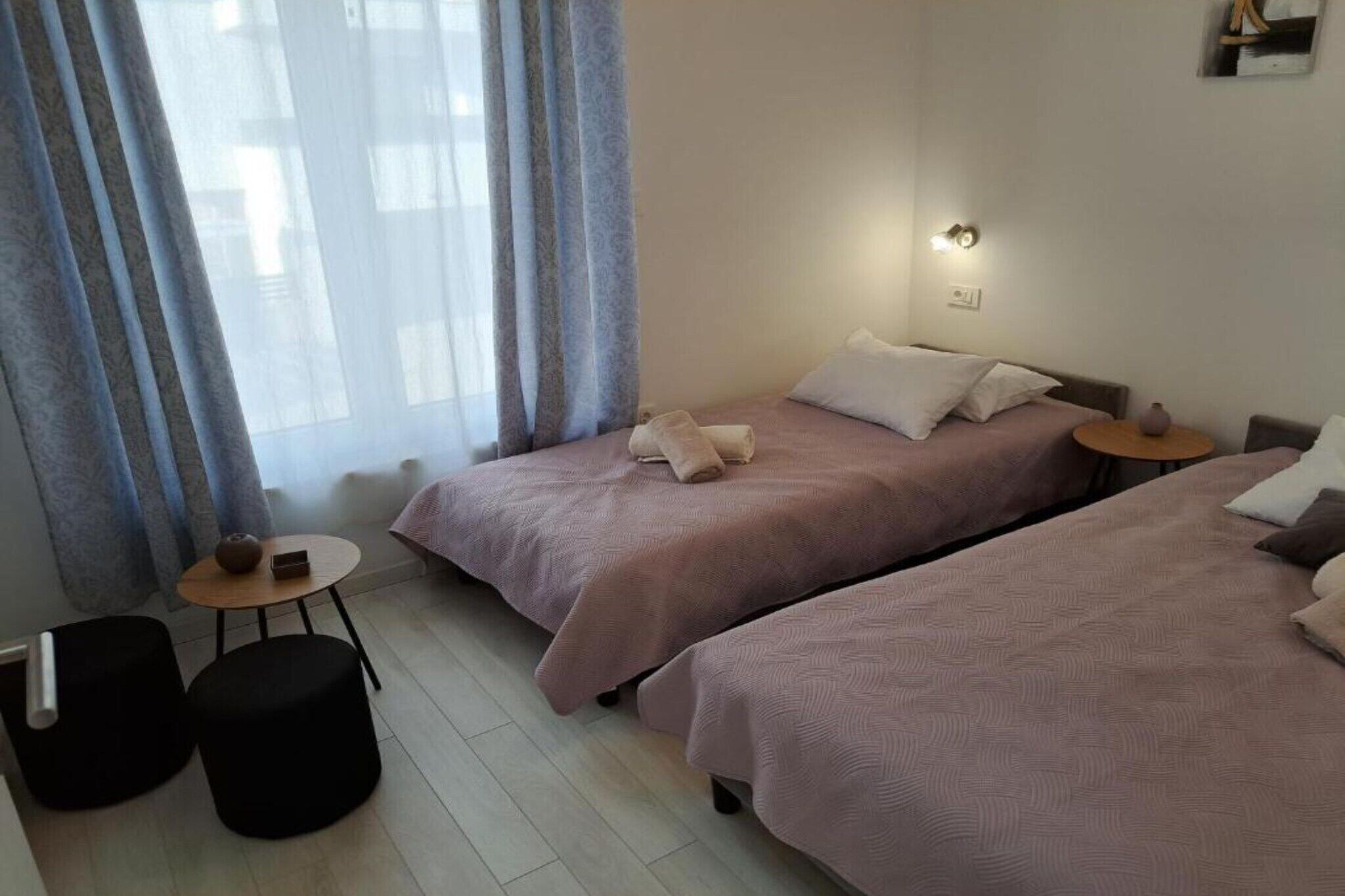 Ein Hotelzimmer mit zwei Betten, einem kleinen Tisch mit einer Vase und einem Fenster mit Vorhängen.