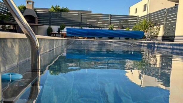 A swimming pool with a clear blue water surface, a blue pool cover, and a metal ladder. - Elegant Villa Ilma with Pool - Villa With Pool (Vodice)