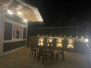 An outdoor patio area with a stone wall, seating, and a bar counter with lights. - Orchard Hill Retreat (Dhari)