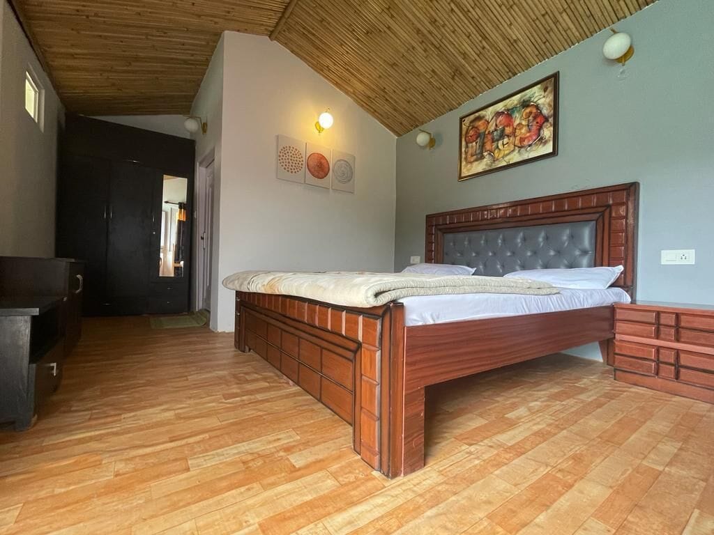 Un dormitorio con piso de madera, una cama con cabecera, un aparador y un cuadro en la pared.
