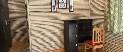 A room with a wooden floor, a desk with drawers, a chair, and a bed.