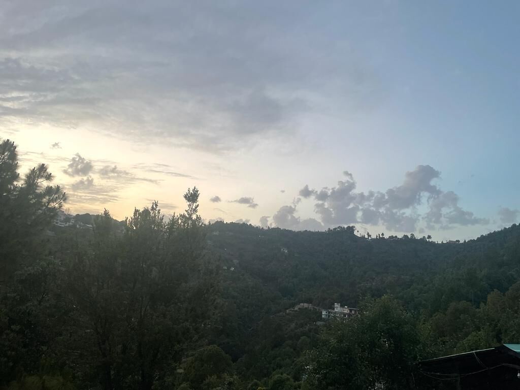 Un paisaje montañoso con bosque denso y un edificio solitario a lo lejos.