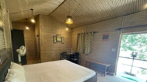 Een slaapkamer met een bed, een ventilator, een bankje en uitzicht op de omgeving.