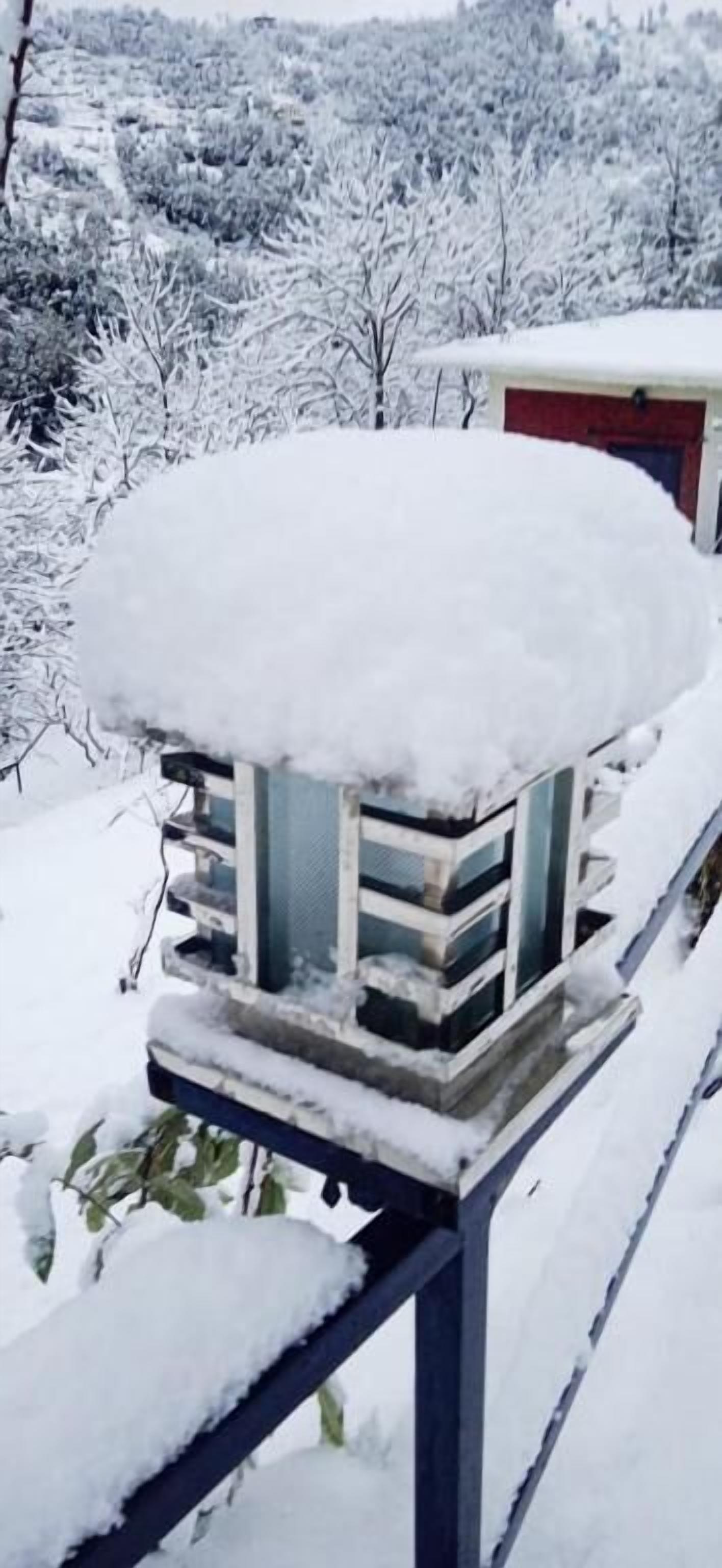 A snow-covered outdoor structure, possibly a gazebo or a small pavilion, with a metal railing and a flat roof.