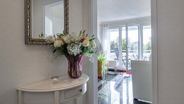 A bathroom with a white vanity, a mirror, and a vase of flowers. - Sand - Lust auf Sylt - Sand vacation apartment for 2 people (Sylt-Ost)