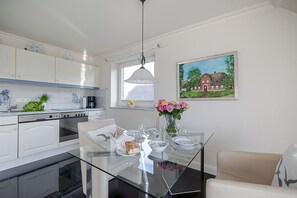 Una cocina moderna con armarios blancos, una mesa de comedor de vidrio y un cuadro con una casa en la pared.