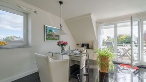 A modern kitchen with a glass dining table, white chairs, a large window, and a view of the outdoors. - Sand - Lust auf Sylt - Sand vacation apartment for 2 people (Sylt-Ost)