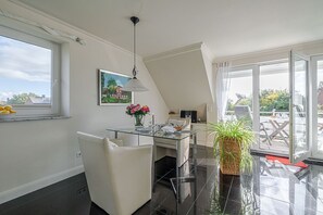 A modern kitchen with a glass dining table, white chairs, a large window, and a view of the outdoors. - Sand - Lust auf Sylt - Sand vacation apartment for 2 people (Sylt-Ost)
