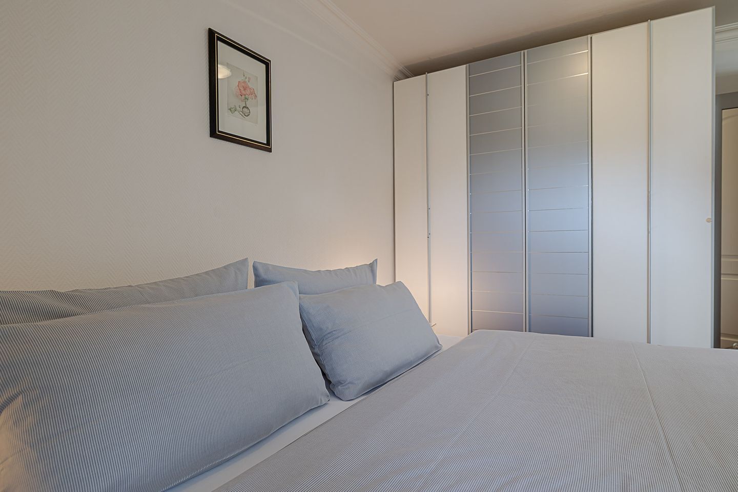 Ein Schlafzimmer mit einem Bett, Kissen, einem gerahmten Bild an der Wand und einem Schiebetürenschrank.