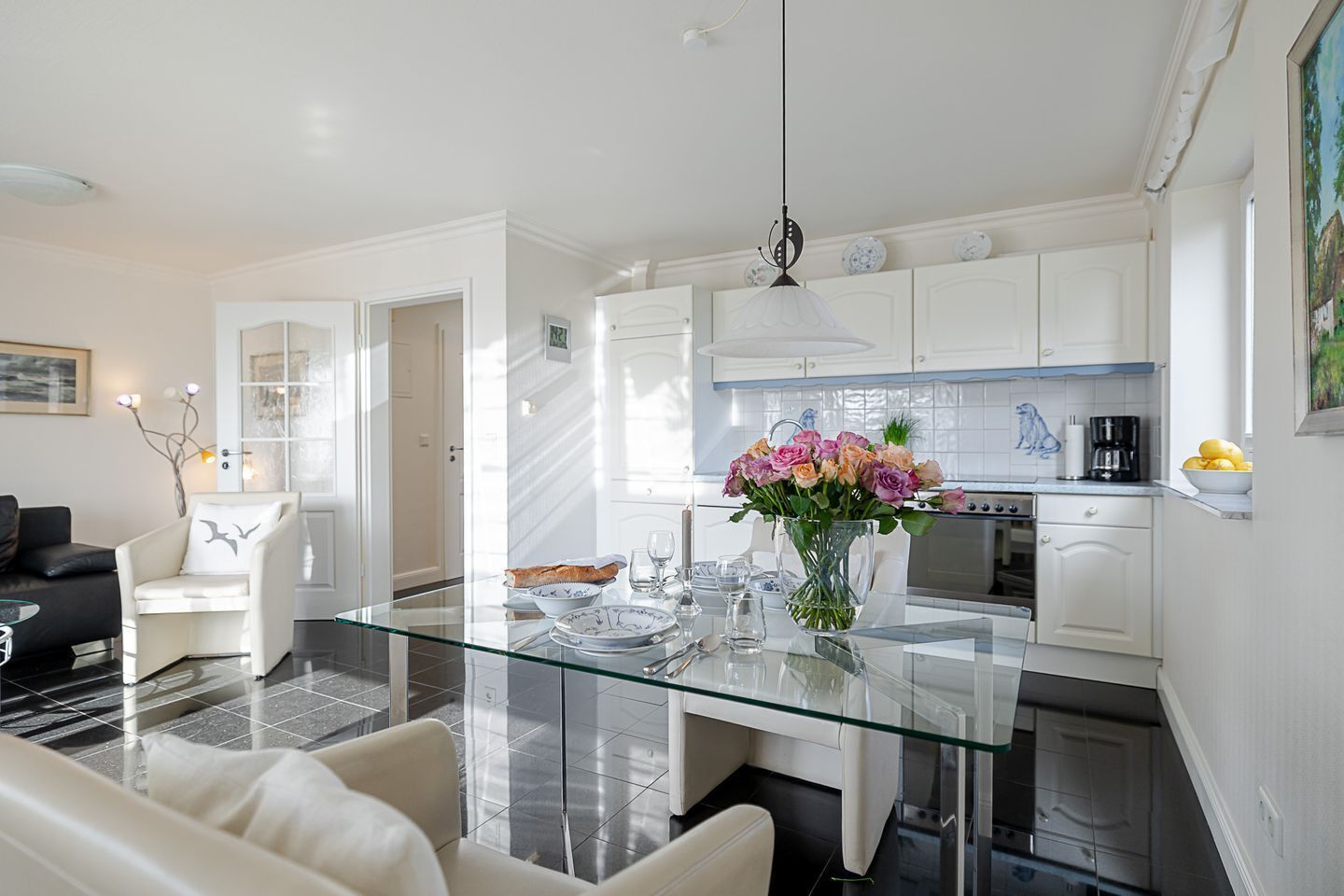Une cuisine moderne avec des meubles blancs, une table à manger en verre et un vase rempli de fleurs.