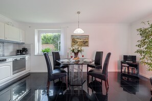 A modern kitchen with a dining area, featuring a black dining table, four chairs, a coffee maker, and a painting on the wall. - Möwe - Lust auf Sylt - Holiday apartment Möwe for 2 persons (Sylt-Ost)