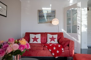 Un divano rosso con cuscini a forma di stella, un quadro raffigurante un paesaggio marino e un vaso di fiori.