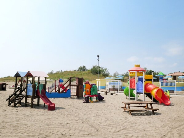 A beach playground with various play structures, including slides and climbing areas, and a picnic table.