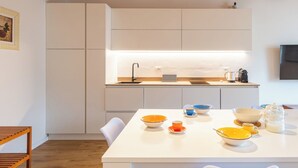 A modern kitchen with white cabinetry, a wooden ceiling, and a dining area with a table set for four. - Vista Lago Consolini by Interhome (Brenzone)