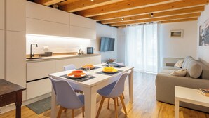 A modern kitchen with a dining area, wooden ceiling beams, a flat-screen TV, and a sofa in a living space. - Vista Lago Consolini by Interhome (Brenzone)