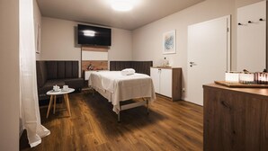 Quarto de hotel com cama, uma mesinha com xícara e pires, sofá, televisão na parede e aparador de madeira com espelho.